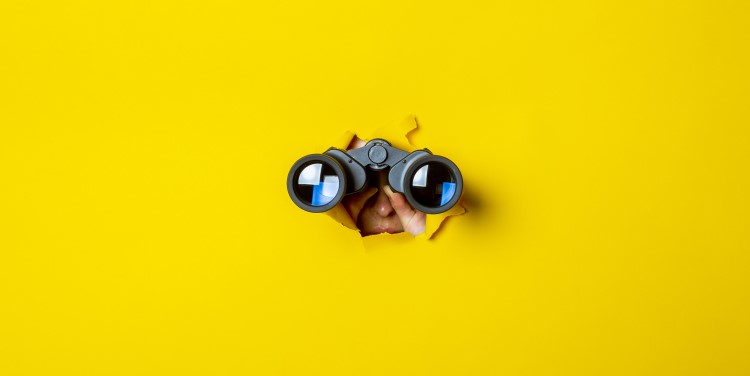 hand holding black binoculars on a yellow background